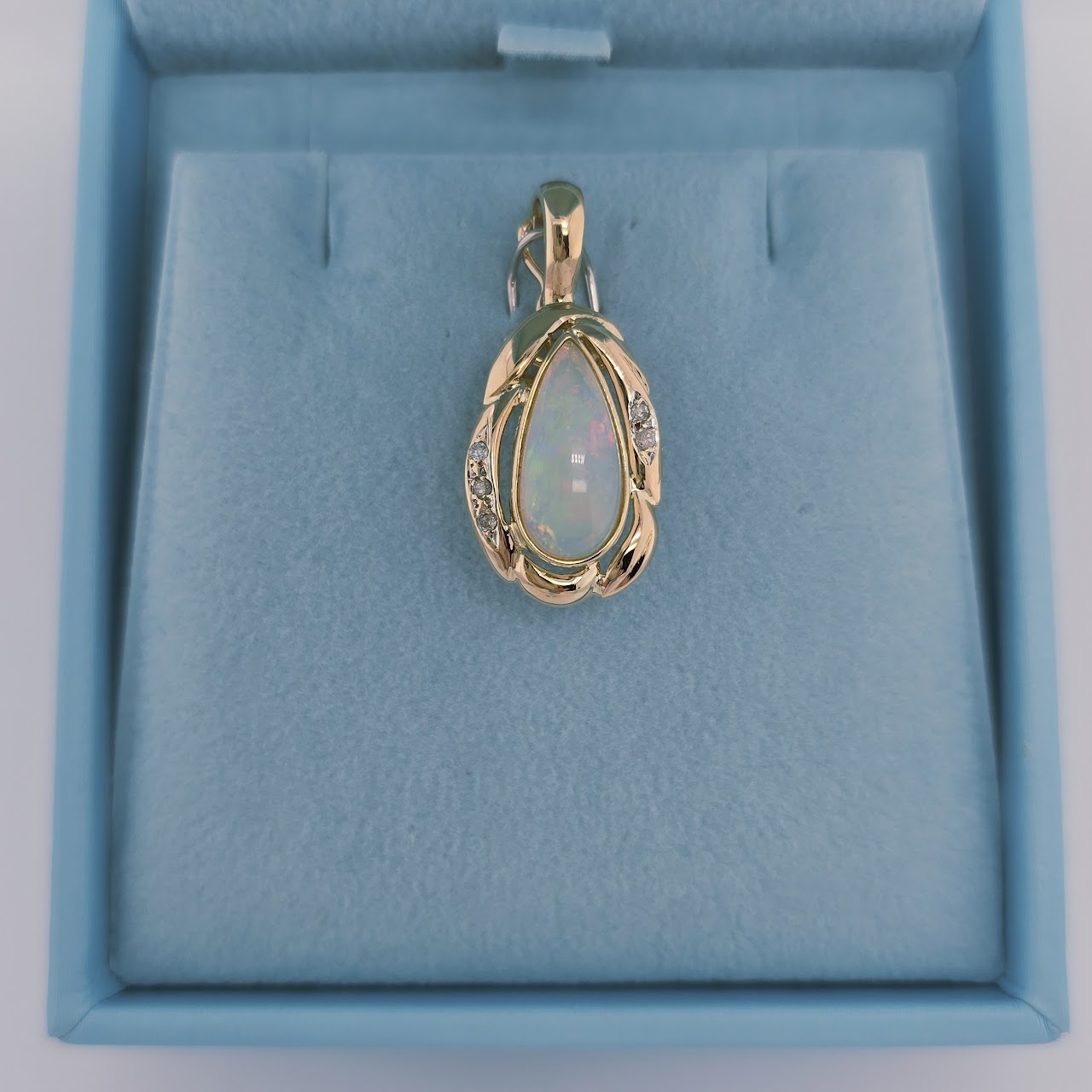 14k yellow gold pendant with a pear-shaped cabochon opal and round diamond accents, designed with a freeform setting and hinged bail for omega chains.