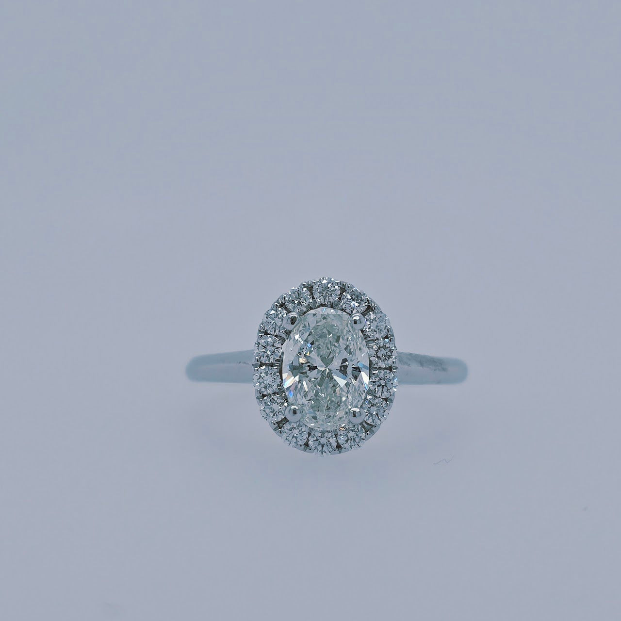 Close-up of a 1.00 carat oval diamond halo engagement ring in 14k white gold, featuring a plain polished shank and GSI-certified center diamond with sparkling halo.