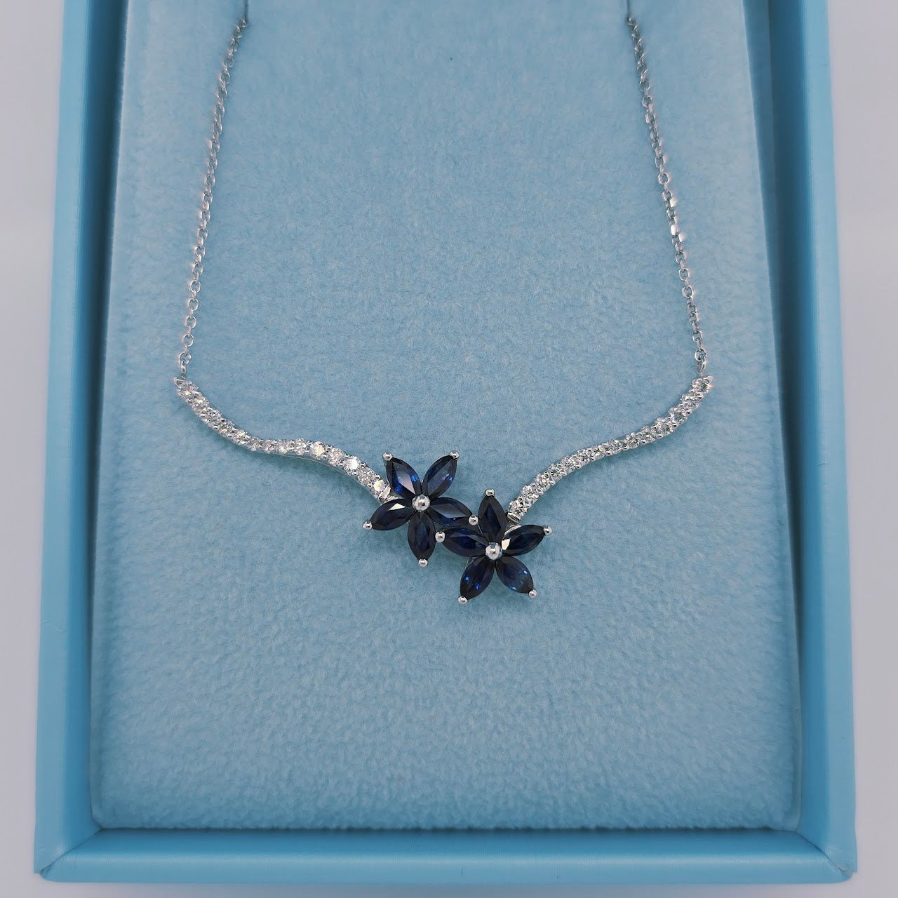 Elegant 14k white gold sapphire and diamond necklace with two floral clusters in a toi et moi design. Features marquise-cut sapphires and diamond-accented stems on an 18-inch cable link chain.