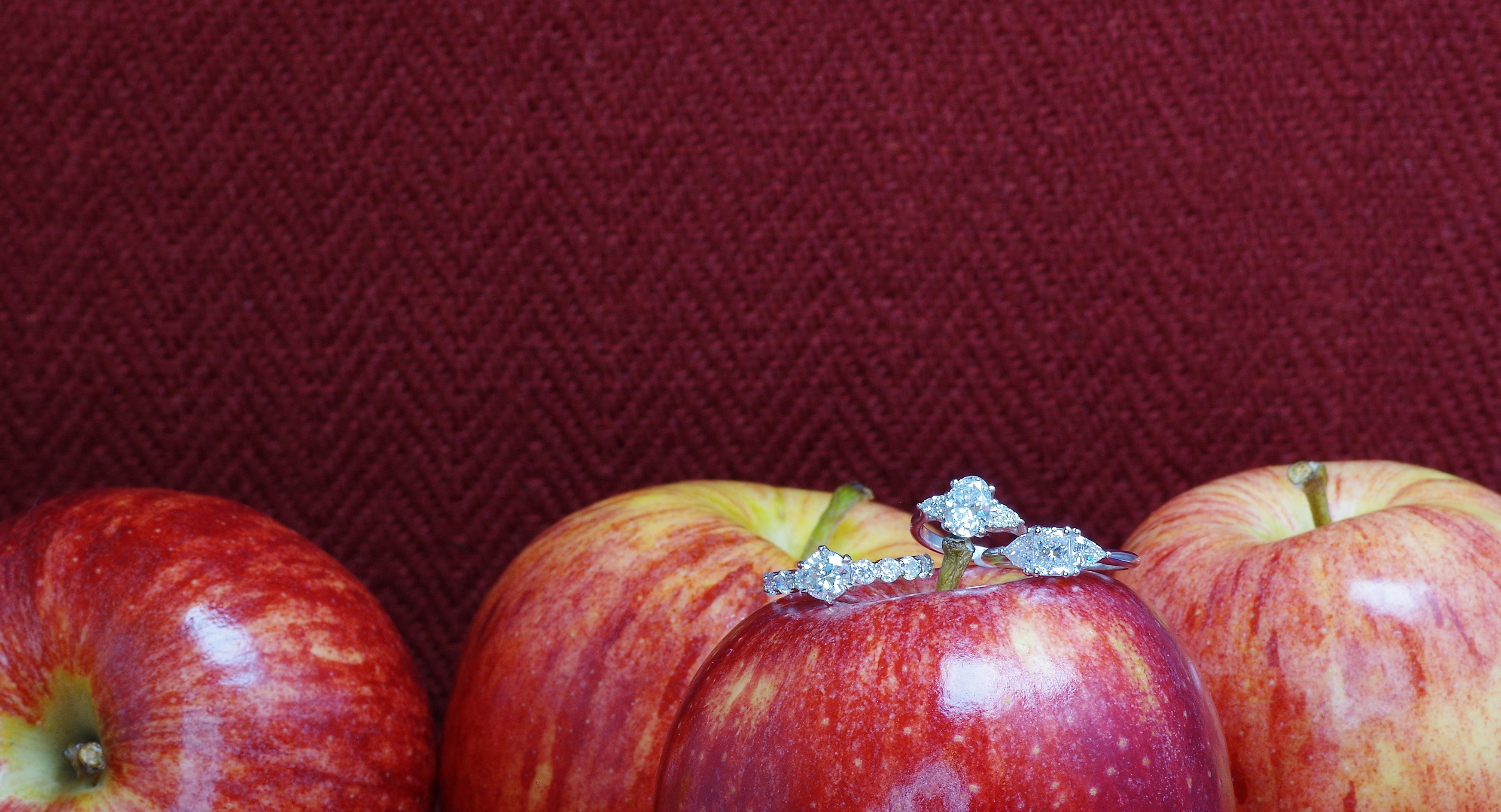 Three red apples with diamond rings on one of them against a red background