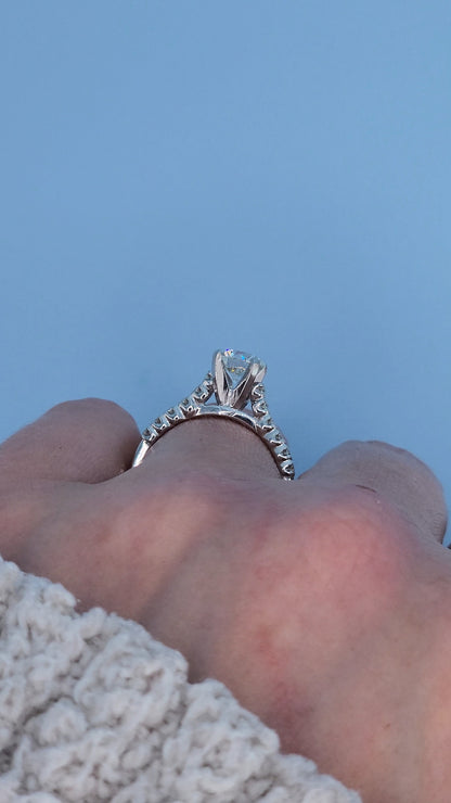 Side view of a white gold engagement ring with a diamond on a finger against a blue background.