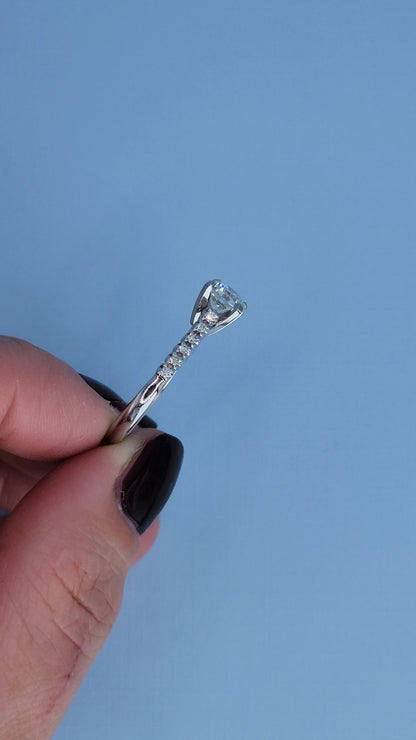 White gold engagement ring with a diamond held by a hand against a blue background