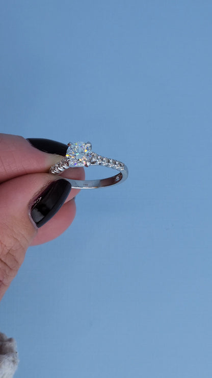 Classic engagement ring with a diamond held by a hand against a blue background