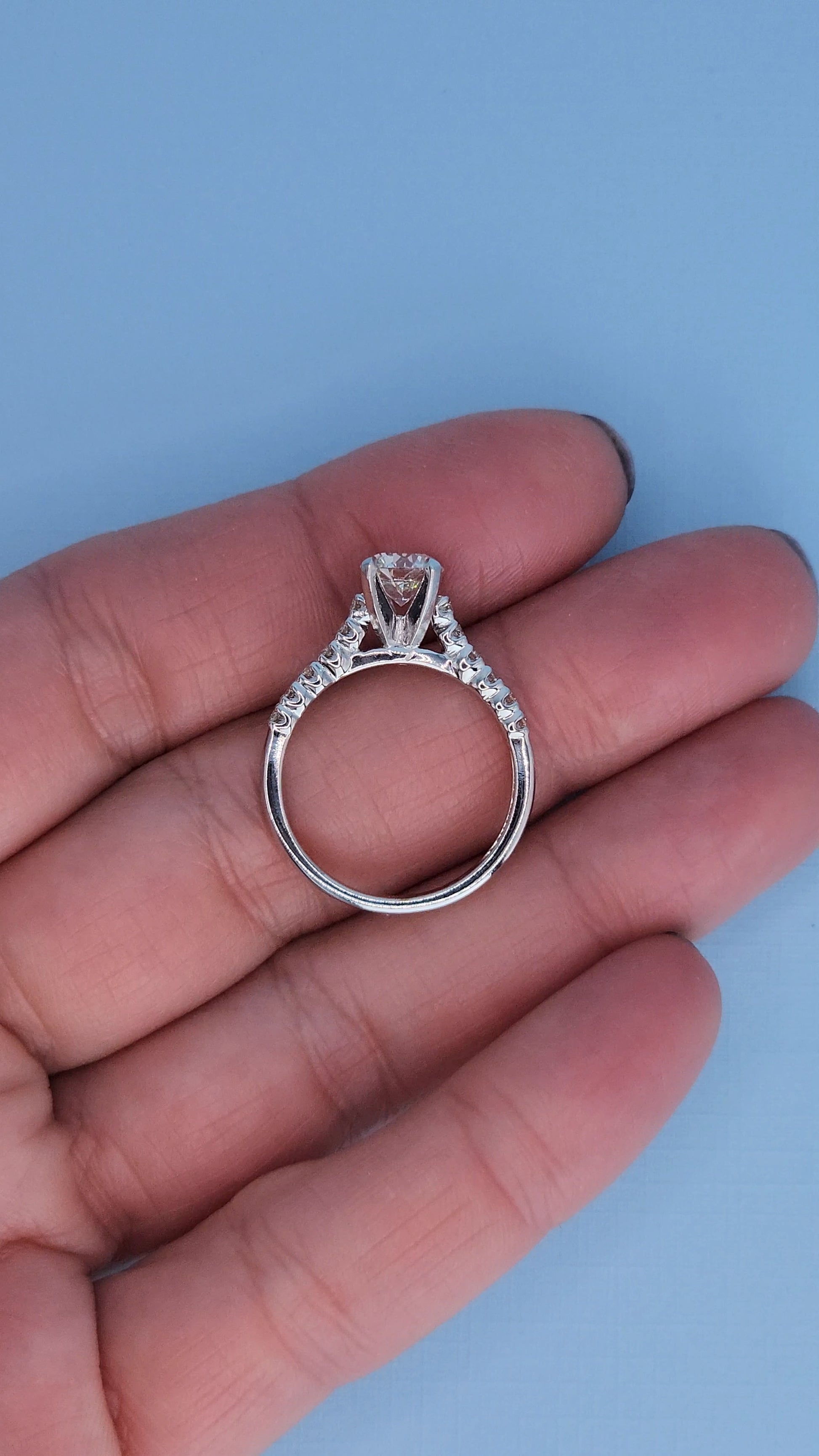 Diamond ring held in a hand against a light blue background
