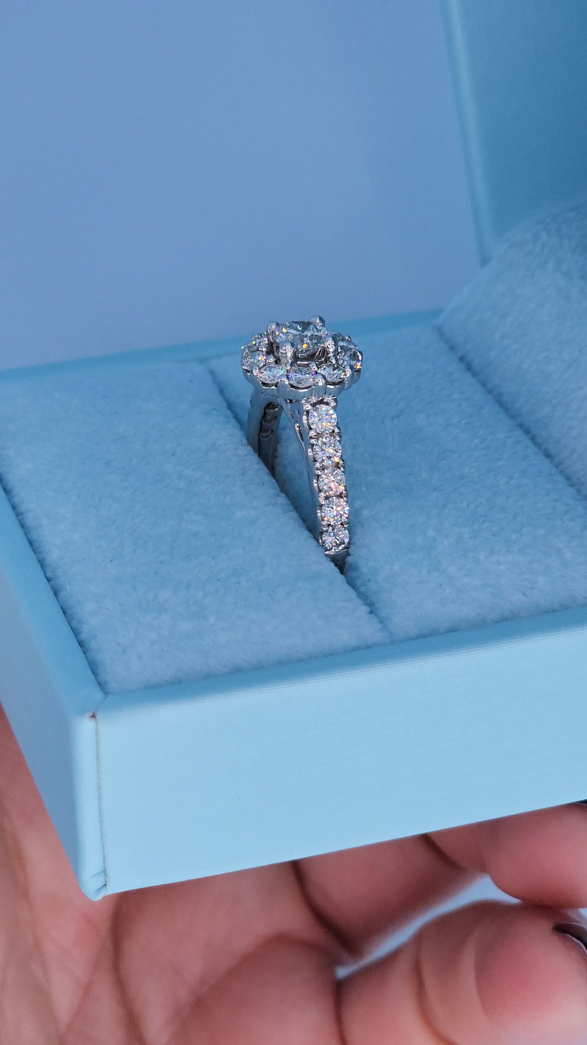Diamond ring in a light blue jewelry box held by a hand.