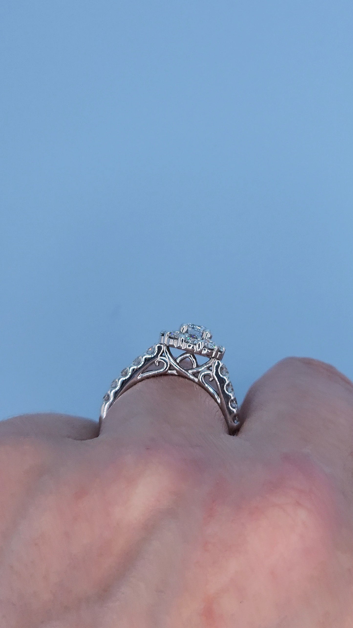 Ladies diamond ring with intricate design on a finger against a light blue background