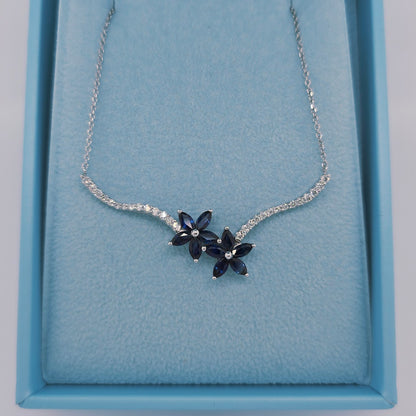Elegant 14k white gold sapphire and diamond necklace with two floral clusters in a toi et moi design. Features marquise-cut sapphires and diamond-accented stems on an 18-inch cable link chain.